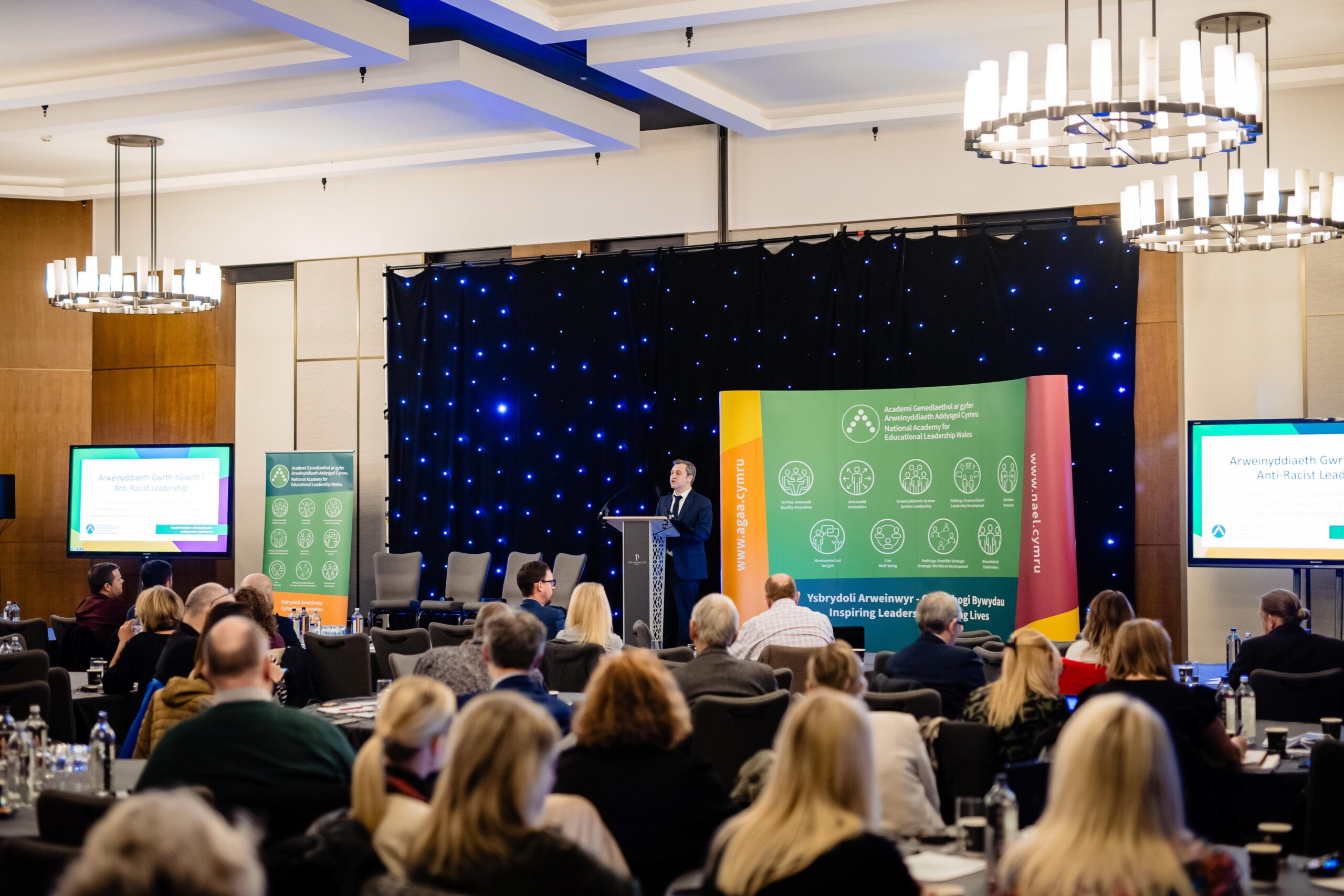 An educational leader standing at a podium at a National :Leadership Conference in front of a crowd of people
